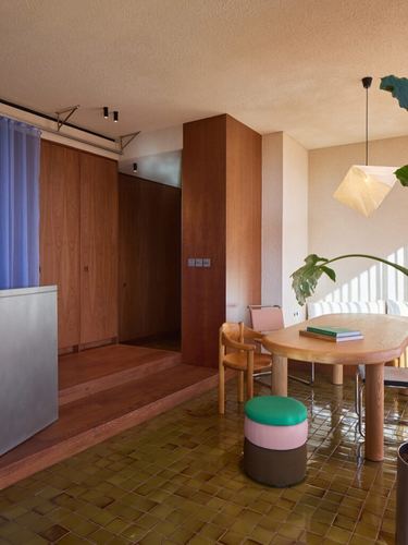 Dining nook with round wood table, green glazed tile floor, and wood wardrobe wall on a raised platform