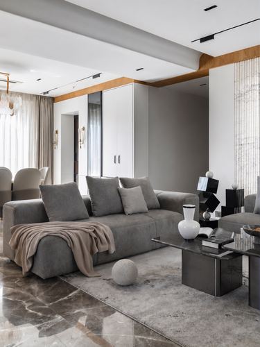 Grey sectional sofa with taupe throw beside a dark metal coffee table on a marble floor