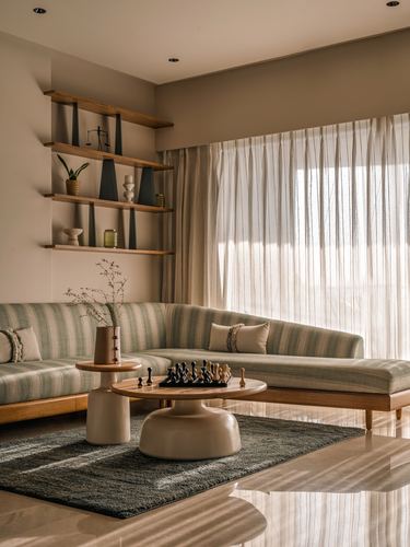 Living room corner with striped sectional sofa, round coffee table with chess set, and sheer curtains.