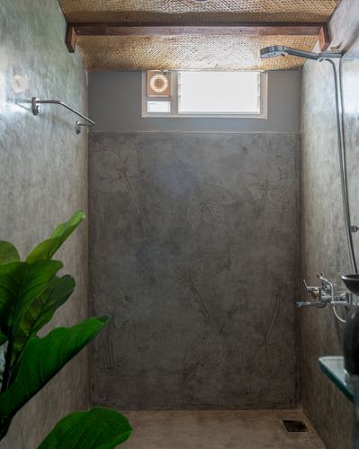 Concrete shower stall with etched leaf motifs, woven ceiling, small window and green plant
