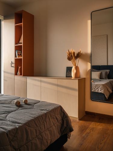 Bedroom corner with terracotta shelving, fluted cabinet, leaning mirror and sunlit wooden floor