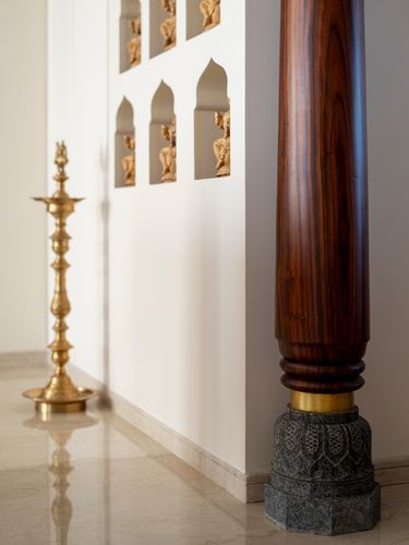 Turned wood column on carved stone base beside brass lamp and niches with brass figurines