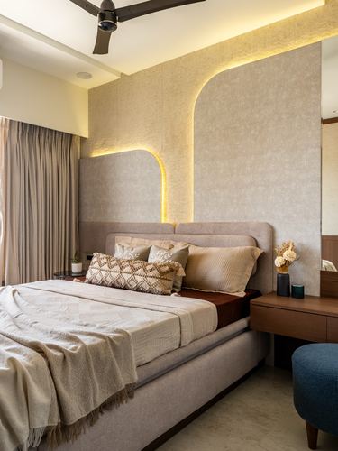 Beige upholstered bed against textured wall with arched backlit niches and wooden bedside table