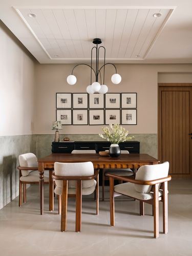 Dining room with wooden table, cane-back chairs, black sideboard and gallery wall under globe chandelier