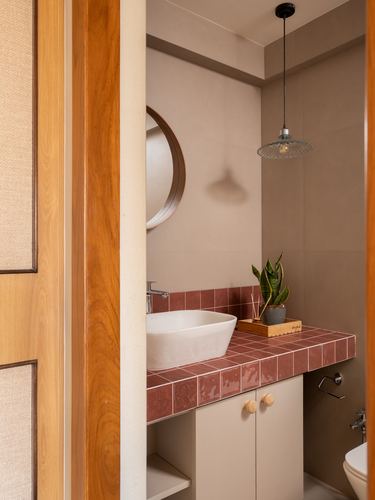 Terracotta-tiled bathroom vanity seen through wooden door frame, with round mirror and pendant light