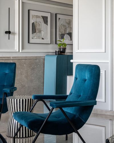 Teal velvet armchairs beside striped stool in a paneled living room