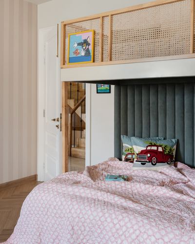 Child's bedroom with pink quilted bed, tufted green headboard, and cane-railed bunk loft above