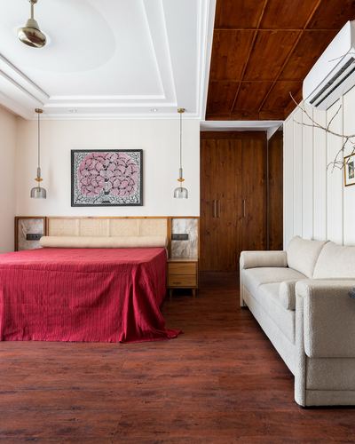 Bedroom with red bedspread, cane headboard, wooden ceiling nook and adjoining lounge with boucle sofa
