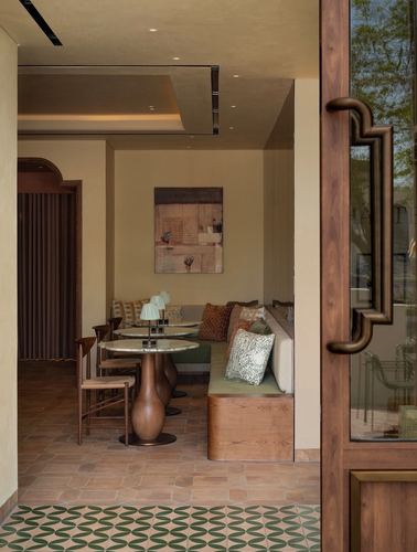 View through a wooden framed glass door into a café seating nook with terracotta floor and banquette.