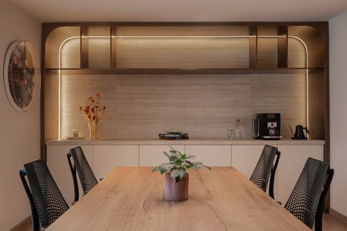 Dining table with mesh chairs facing a backlit stone credenza with arched bronze trim