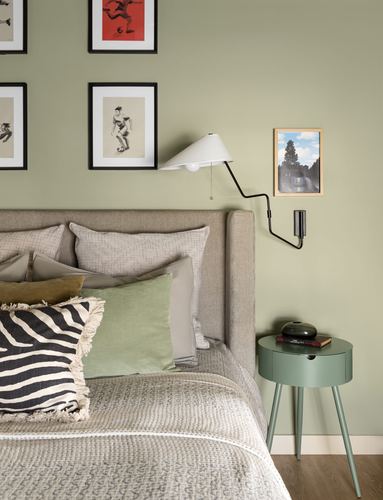 Sage green bedroom with upholstered headboard, gallery frames, and round green nightstand