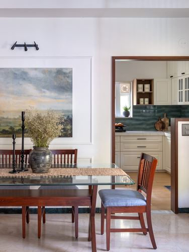 Dining table with glass top and wooden chairs facing an open kitchen with green tiled backsplash