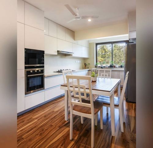 White gloss kitchen with built-in oven, wood-look tile floor, and small dining table with mixed chairs