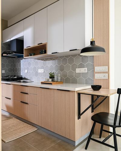 Modern kitchen with grey hexagonal tile backsplash, wood cabinetry, and a black pendant light over a fold-down table