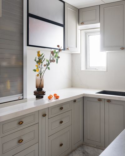 L-shaped kitchen with grey cabinetry, marble-look counter, vase of branches and citrus fruit