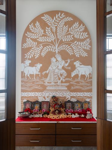 Pooja niche with terracotta mural of Radha Krishna above wooden altar with idols