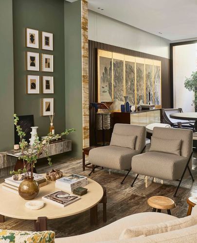 Living room with olive wall, gallery frames, striped chairs, and backlit stone divider