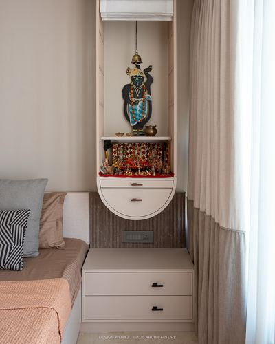 Small arched pooja niche with deity figure built into bedroom nightstand unit, curtains beside