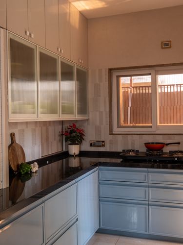 L-shaped kitchen with blue cabinetry, dark stone counters, and ribbed glass upper cabinets under a window