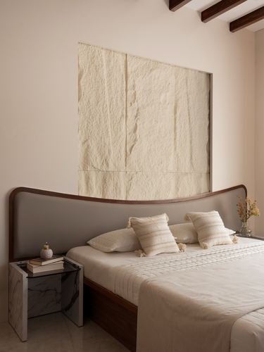 Bedroom with curved wood-and-leather headboard beneath a textured recessed wall panel and marble side table