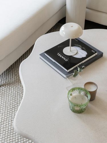 Overhead view of a wavy plaster side table styled with books, a lamp, and candles beside a sofa