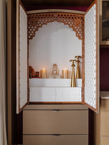 Open wooden mandir cabinet with carved arched doors, idol, candles and brass diyas above drawers