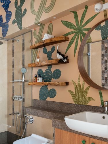 Bathroom with cactus mural, floating wood shelves holding a cat figurine, round wood-framed mirror, and stone counter with sink