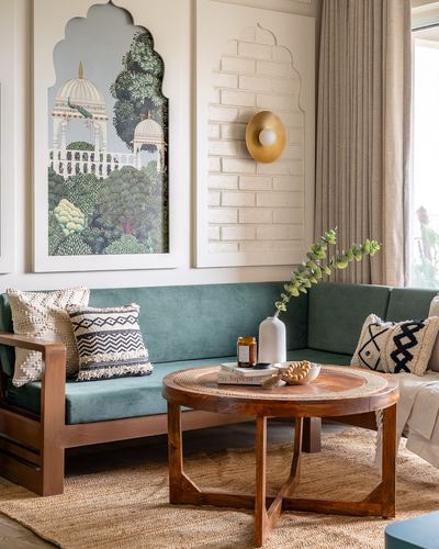 Teal velvet sectional sofa with round teak coffee table beneath arched artwork and brass sconce