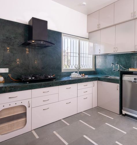 L-shaped kitchen with green stone counters, white cabinetry, black chimney hood, and a cane-front drawer