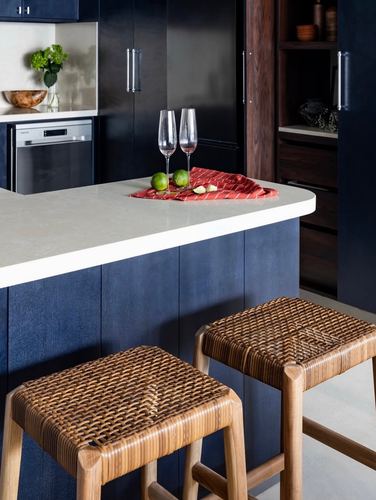 Indigo kitchen island with pale stone counter, wine glasses, and two woven cane stools