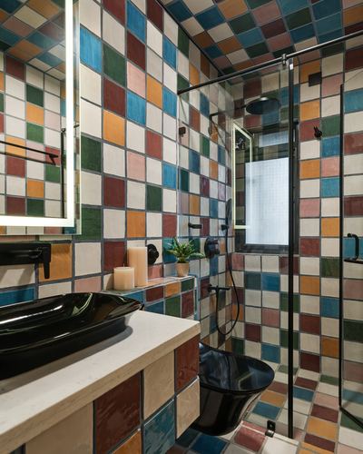 Bathroom fully tiled in multicolor checkerboard pattern with black fixtures and glass shower