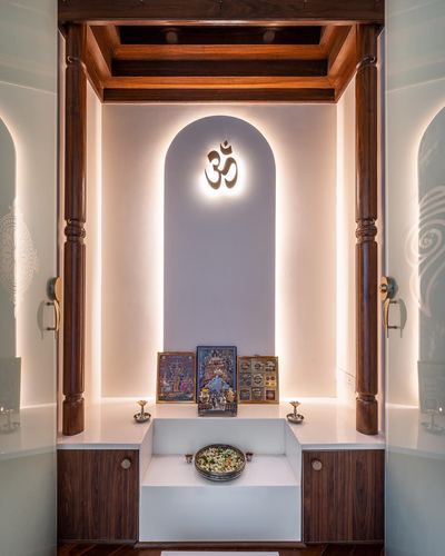 Pooja room with carved wooden pillars and backlit arched niche glowing om symbol