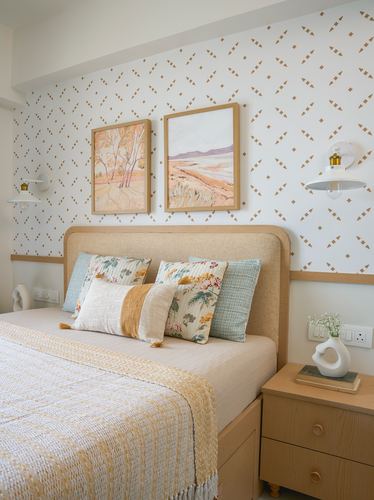 Bedroom with patterned wallpaper, upholstered headboard, layered pillows, and wooden nightstand