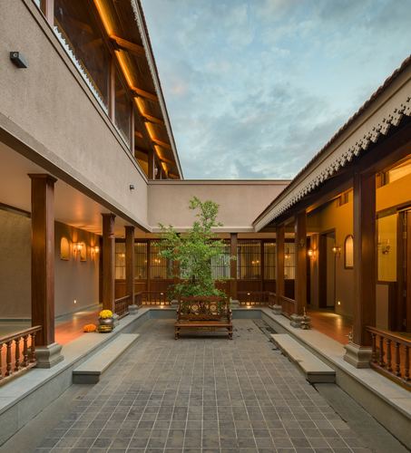 Traditional Maharashtrian wada courtyard with teak columns, sloping roofs, and central tree at dusk