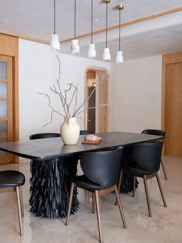 Dining table with sculptural black textured base, black leather chairs, and cluster pendant lights near an arched doorway