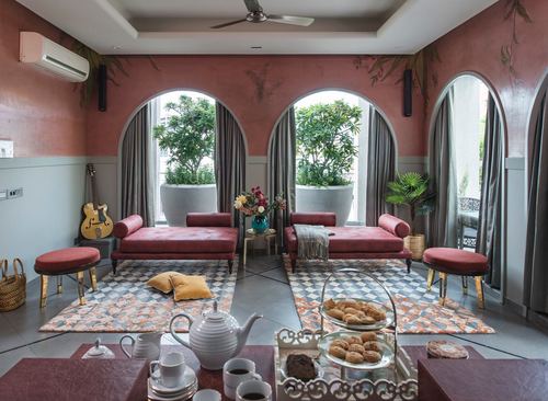 Pink-walled living room with arched windows, rose velvet chaises, and patterned rugs in Jaipur home