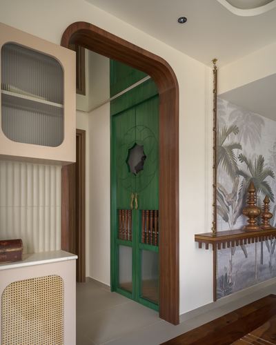 Arched wooden doorway with green carved door beside a console and palm-print wallpaper wall
