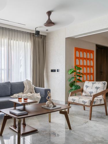 Living room with grey sofa, wooden coffee table, printed armchair, and orange arched jali wall panel