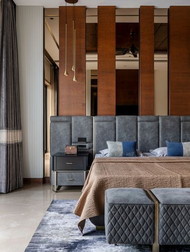 Bedroom with tufted grey headboard, wood-mirror panelled wall, and two bronze pendant lights