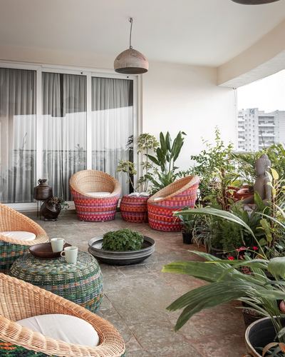 Balcony seating with cane chairs and woven stools surrounded by potted plants and city view