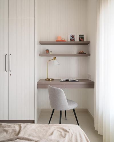 Small study nook with floating desk, shelves, brass lamp and grey chair in a white paneled corner