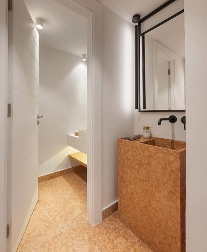 Minimalist bathroom with textured ochre stone sink and black-framed mirror, seen through open doorway.