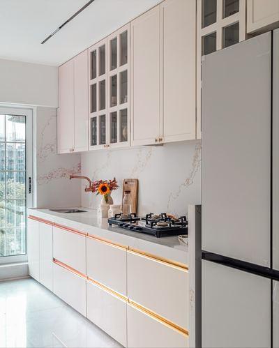 Galley kitchen with beige marble-look backsplash, white cabinetry with gold trim, and gas hob