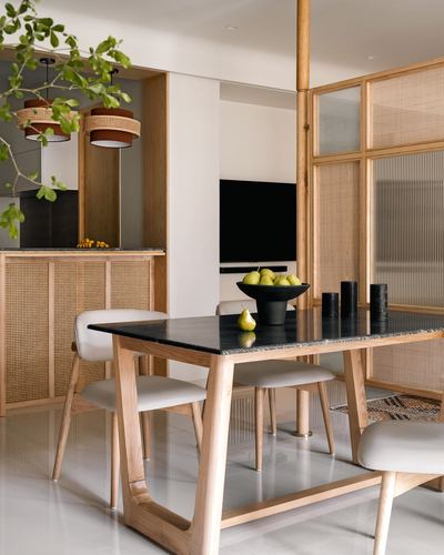 Wooden dining table with cane pendant lights and cane partition wall in a minimalist Japandi dining space