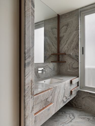 Marble-clad bathroom corner with floating vanity, brass accents, and frosted window light