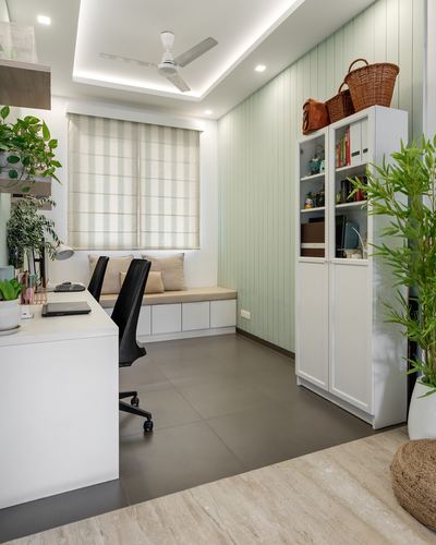 Home office with green paneled wall, window seat, white desk and storage cabinet