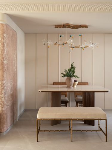 Beige dining nook with marble-look table, cane chairs, brass bench, and branch chandelier