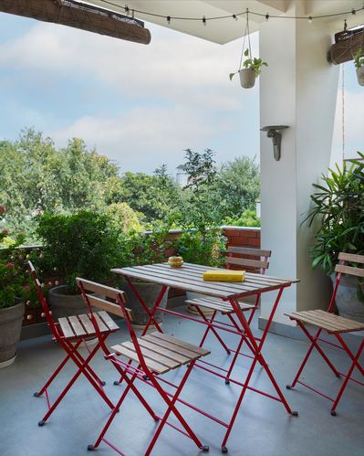 Red folding bistro table and chairs on a covered terrace overlooking trees in Jaipur