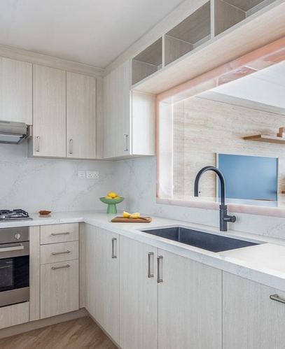Light wood U-shaped kitchen with white stone countertops and a pass-through window above the sink
