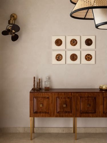 Wooden sideboard with brass legs beneath six circular wall artworks in a plastered foyer